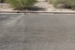 Textured asphalt surface after milling removal next to desert creosote shrubs in Surprise, AZ.
