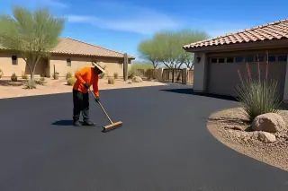 Worker brushing loose aggregate from a finished asphalt driveway in Surprise, AZ.