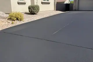 Fresh asphalt overlay with visible seams next to river rock landscaping at a home in Surprise, AZ.