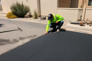 Service professional inspecting fresh asphalt seams by a stucco wall in Surprise, AZ.