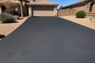 Newly sealcoated black asphalt driveway bordered by desert river rock in Surprise, AZ.