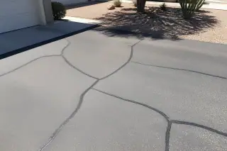 Cured rubberized sealant filling narrow pavement cracks on a residential driveway in Surprise, AZ.