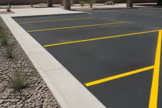 Fresh yellow parking stall lines on dark asphalt with river rock landscaping in Surprise, AZ.