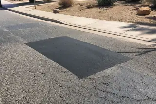 Neatly compacted asphalt patch in a residential driveway surrounded by desert xeriscaping in Surprise, AZ.