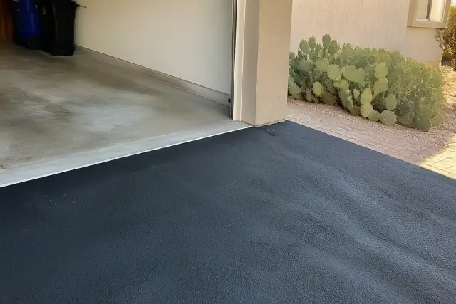 Newly installed residential asphalt driveway meeting a garage slab in Gilbert, AZ, with prickly pear cactus.