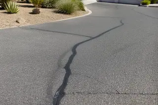 Cured black crack filler in a weathered asphalt surface surrounded by gravel landscaping in Tempe, AZ.