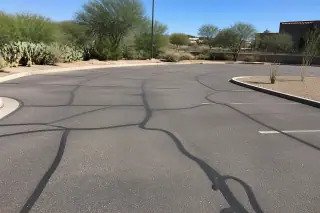 Finished asphalt surface with sealed linear cracks and prickly pear cacti in Tempe, AZ.