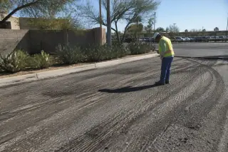 Worker sweeping residual aggregate on a milled asphalt surface near prickly pear cacti in Tempe, AZ.