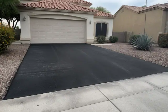 Newly paved asphalt driveway meeting a residential garage in Peoria, AZ, with xeriscaping and a stucco home.