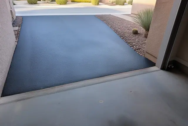 Newly installed asphalt driveway meeting a residential garage slab in Mesa, AZ.