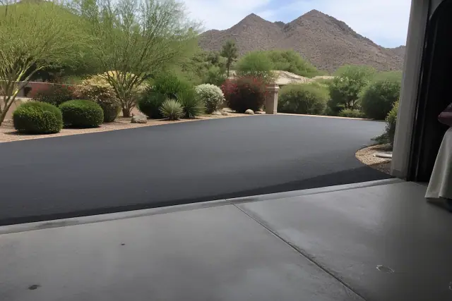 Newly installed asphalt driveway meeting a garage slab in Paradise Valley, AZ, with desert landscaping and mountains.