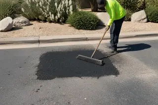 Worker using a push broom to clean a new asphalt patch near prickly pear cacti in Tempe, AZ.