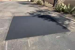 New asphalt patch repair on a commercial pavement edge with prickly pear cacti in Tempe, AZ.