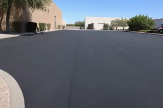 Finished dark asphalt loading zone next to desert landscaping and industrial buildings in Tempe, AZ.