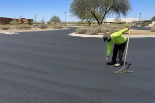 Contractor with a rake inspecting a freshly compacted asphalt surface in Tempe, AZ.