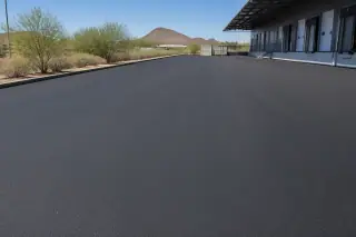 Freshly paved asphalt surface with desert creosote bushes in a commercial loading zone in Tempe, AZ.