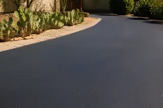 Freshly sealed black asphalt driveway with prickly pear cacti along the edge in Tempe, AZ.