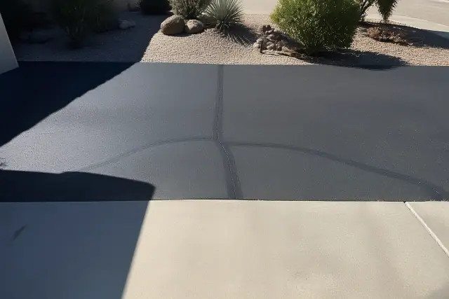 Rubberized crack sealant on an asphalt driveway near a garage slab in Tempe, AZ.