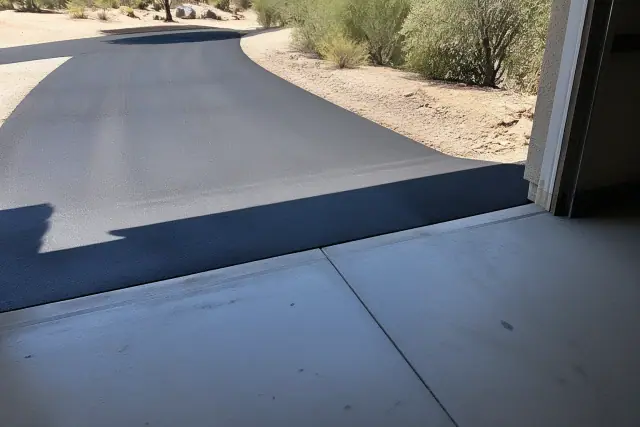 Newly installed asphalt driveway meeting a residential garage slab in Phoenix, AZ.