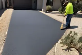 Worker sweeping debris near a finished asphalt driveway with prickly pear cacti in Tempe, AZ.