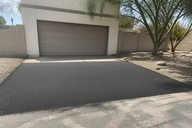 New asphalt driveway transition at a residential property in Tempe, AZ, showing a flush joint against the garage slab.