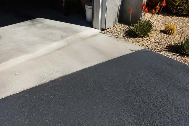 Narrow surface cracks at the transition between a garage slab and new asphalt driveway in Tempe, AZ.