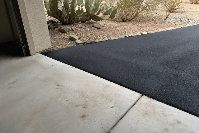 Newly installed asphalt driveway meeting a residential garage slab in Glendale, AZ with desert landscaping.
