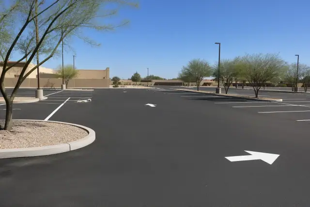 Newly paved asphalt parking lot with painted stall markers and xeriscaping at a retail center in Phoenix, AZ.