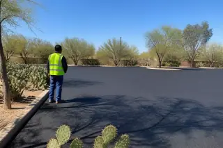 Contractor in a high-vis vest inspecting a smooth asphalt surface with prickly pear cacti in Tempe, AZ.
