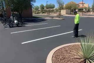 Technician inspecting crisp parking stall lines on fresh asphalt near volcanic rock landscaping in Tempe, AZ.
