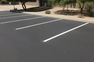 Brightly painted parking stall lines on smooth dark asphalt with desert gravel landscaping in Tempe, AZ.