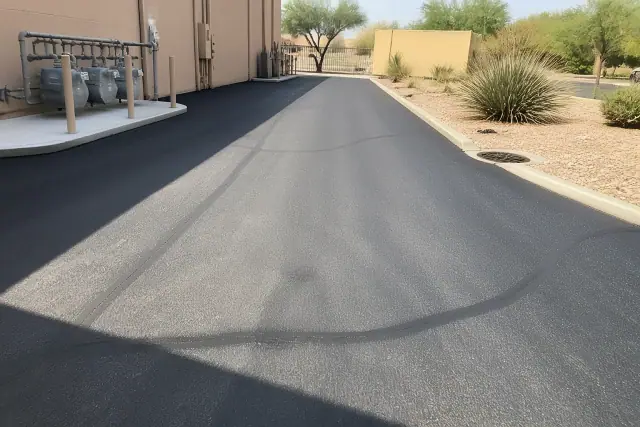 Freshly paved asphalt with repaired cracks at a commercial building utility access point in Tempe, AZ.