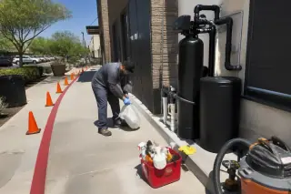 Technician cleaning up near water filtration equipment outside a retail storefront in Tempe, AZ.