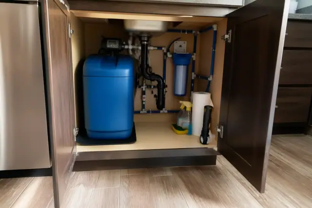 A newly serviced water filtration system with blue softener and clean piping under a kitchen sink in Scottsdale, AZ.