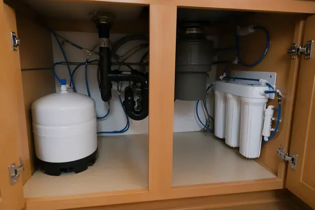 Newly installed water softener and filtration system with blue tubing under a kitchen sink in Surprise, AZ.