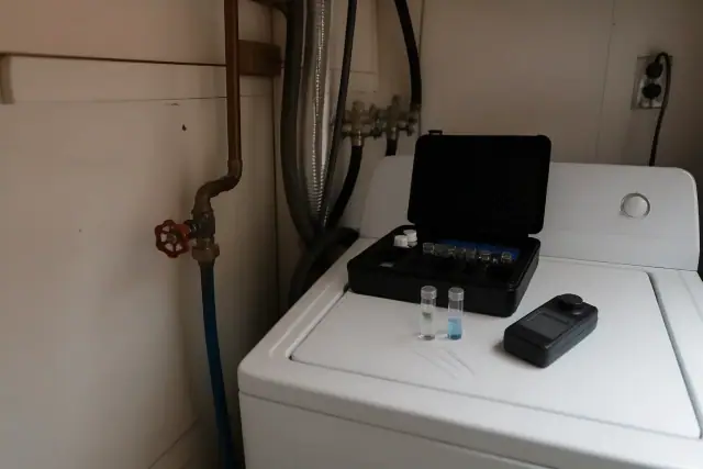 Digital water testing kit with vials and a colorimeter on a washing machine in a Tempe, AZ laundry room.