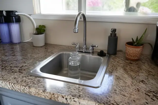 Clear glass water sample bottle under a chrome kitchen faucet on a granite countertop in a home in Tempe, AZ.
