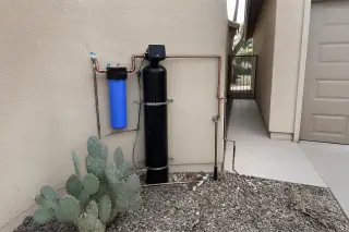 Water filtration hardware with neat piping mounted on a stucco garage wall near a prickly pear cactus in Tempe, AZ.