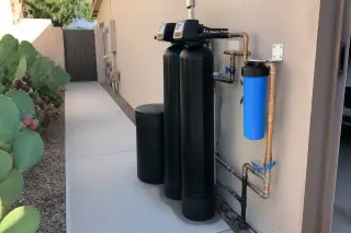 Water filtration system with organized pipes installed beside a stucco garage in a Tempe, AZ yard.