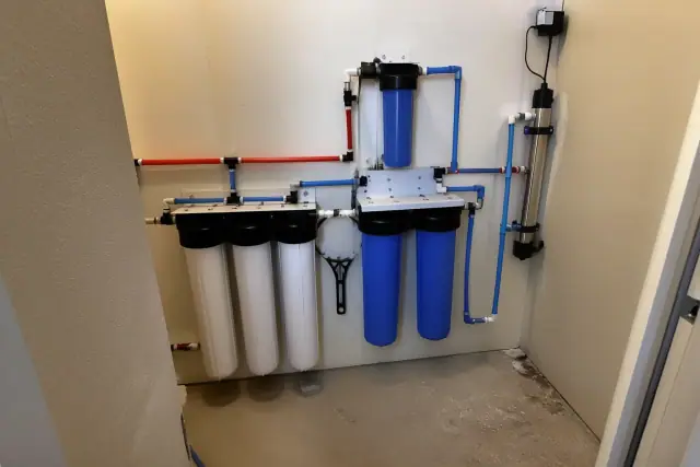 Whole house water filtration system with blue canisters and PEX piping installed in a utility closet in Tempe, AZ.
