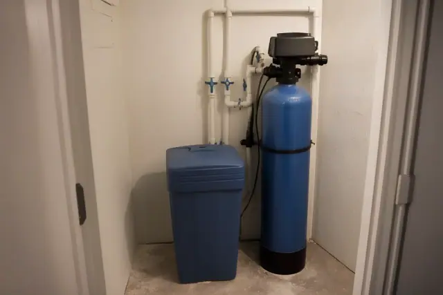Water softener unit with blue tank and PVC piping installed in an apartment mechanical closet in Tempe, AZ.