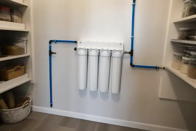 Water filtration system with white filters and blue pipes installed on a residential pantry wall in Goodyear, AZ.