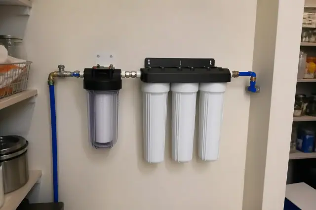 Water filtration system with clear prefilter and PEX plumbing installed on a pantry wall in Mesa, AZ.