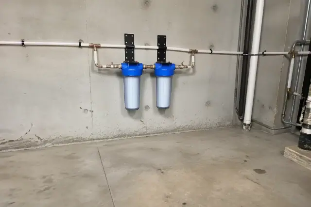 Professional whole-house water filtration system with PEX piping installed on a concrete wall in Tempe, AZ.