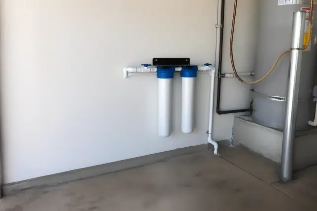 Two sediment filter housings installed on a garage wall next to a water heater in Tempe, AZ.