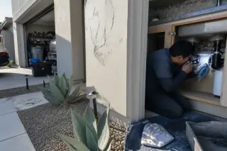 Service professional inspecting under-sink plumbing and pipes in a Tempe, AZ home.
