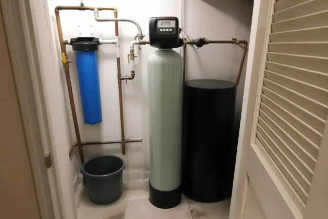 Serviced water softener with copper piping and blue filter housing in an apartment mechanical closet in Tempe, AZ.