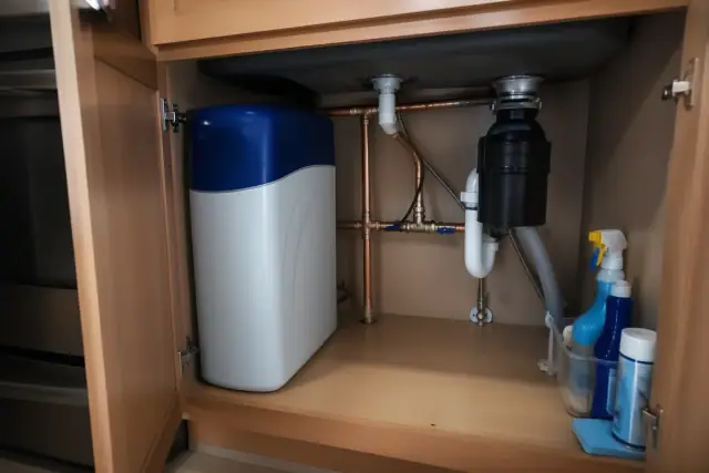 Water softener unit with copper piping installed under a kitchen sink in a Tempe, AZ home.