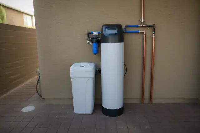 Water softener unit with a white brine tank and copper piping installed on a stucco wall in Avondale, AZ.