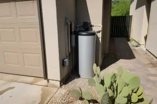 Water filtration unit with plumbing connections beside a garage and prickly pear cactus in Tempe, AZ.